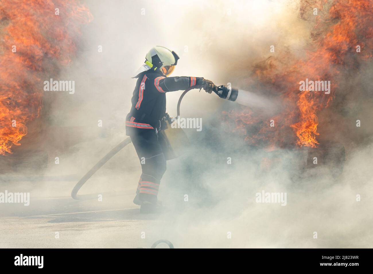 firefighter extinguishes a fire. The hero firefighter stands among the ...