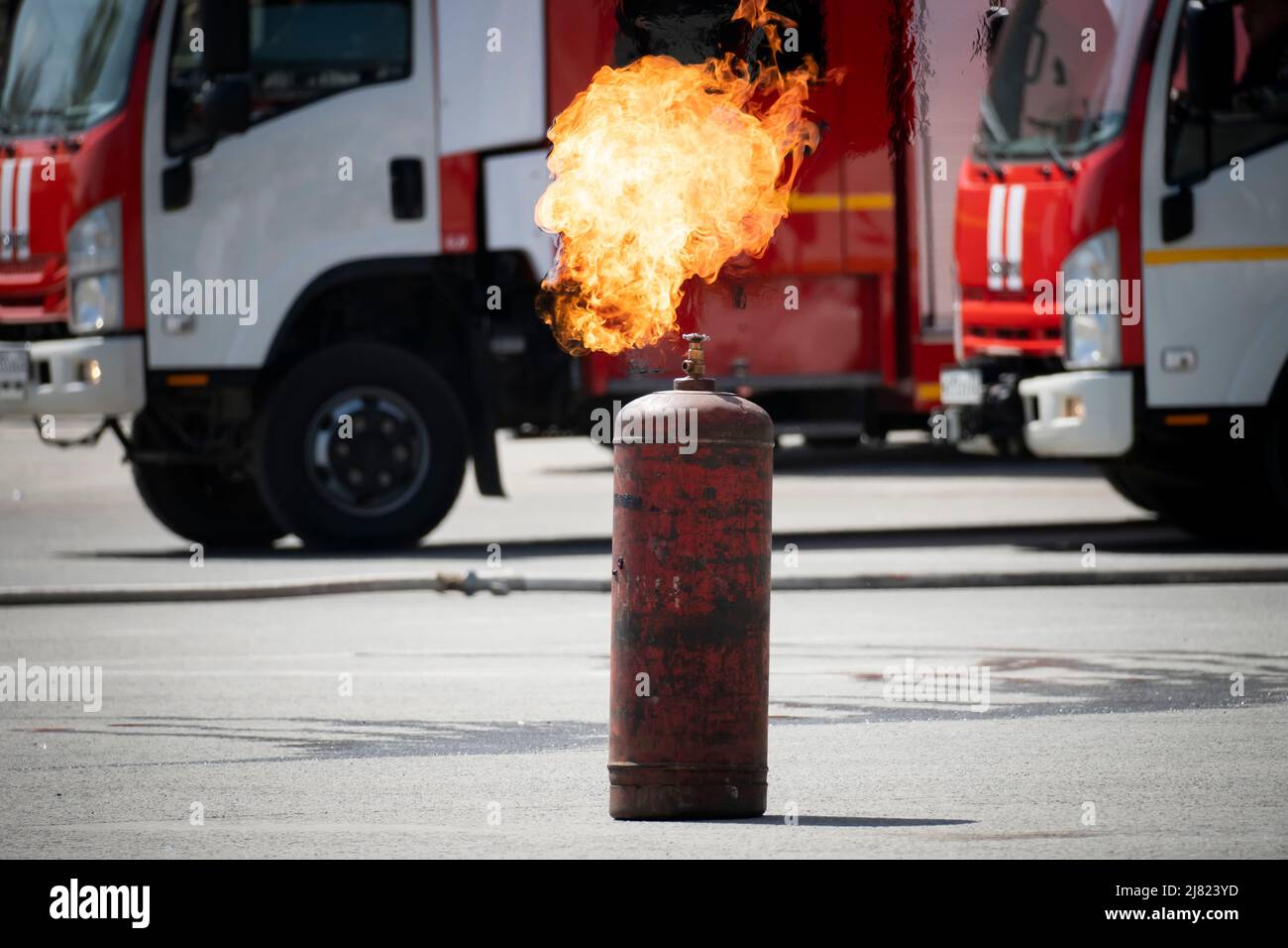 an ignited gas cylinder on the background of a fire truck on the street. Danger of explosion Stock Photo