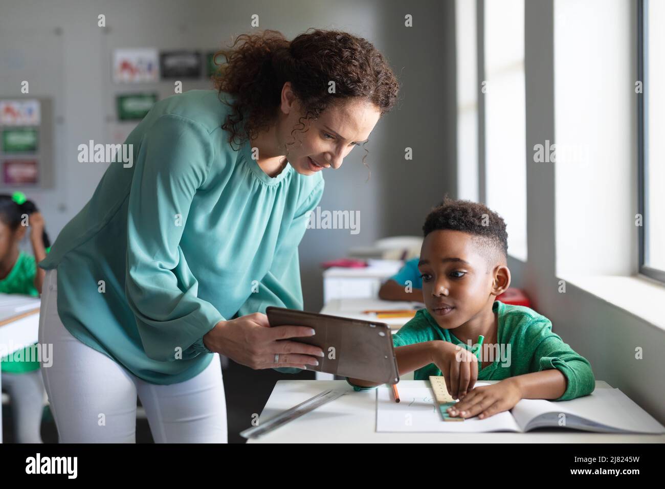 Caucasian young female teacher showing digital tablet to african ...