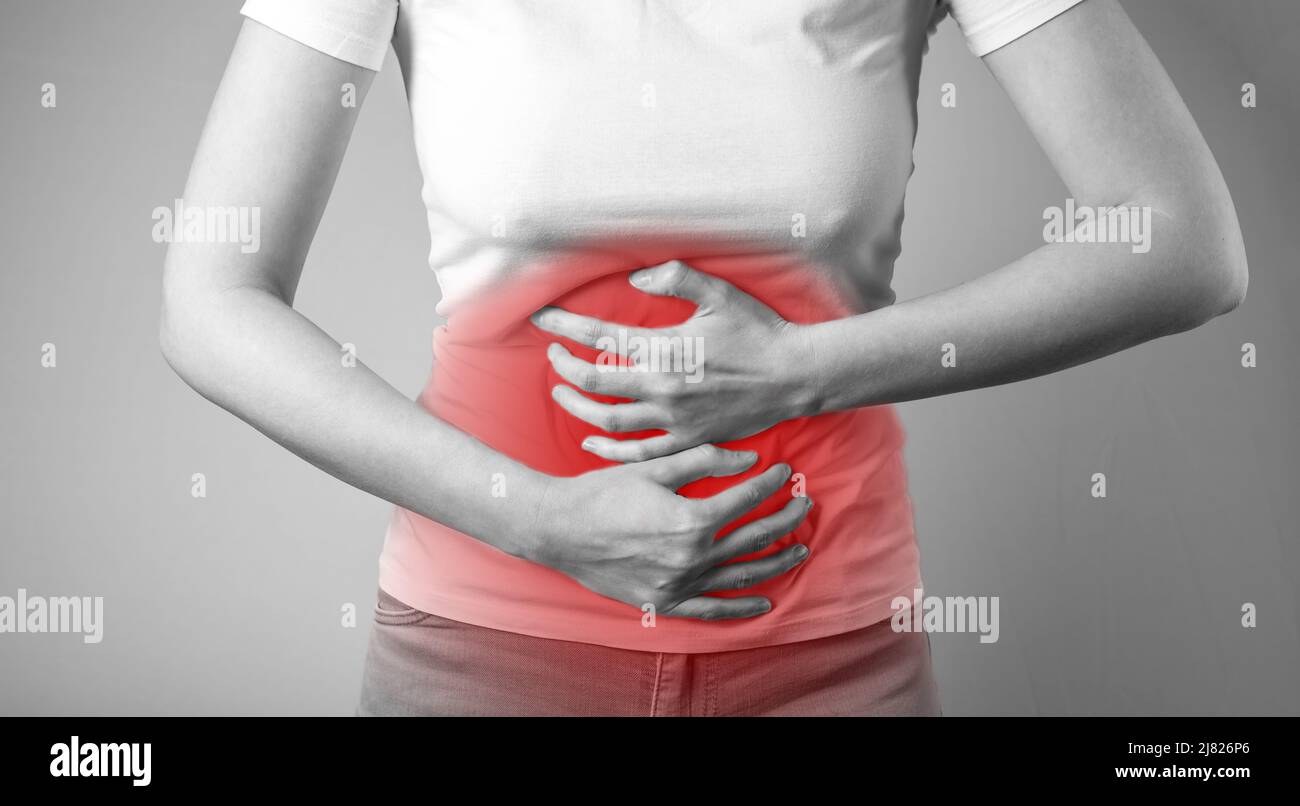 Woman suffering from stomachache. Abdominal pain caused by inflammation, injury, disease. Female holding stomach with red spot. Black and white. High quality photo Stock Photo