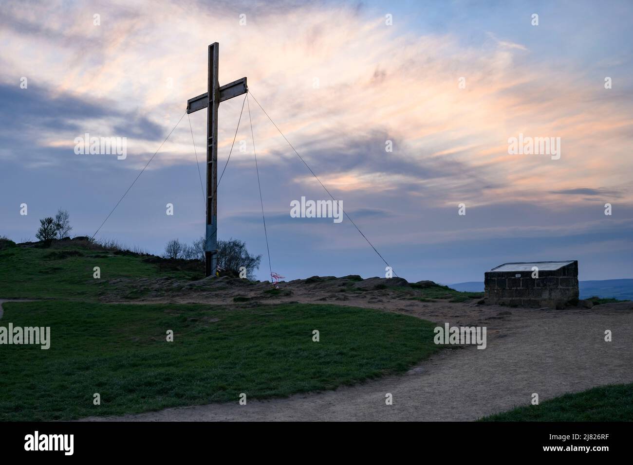 High towering wooden Easter cross (symbol of hope) held with ropes on hilltop & orange red sundown sky - The Chevin, Otley, West Yorkshire England UK. Stock Photo