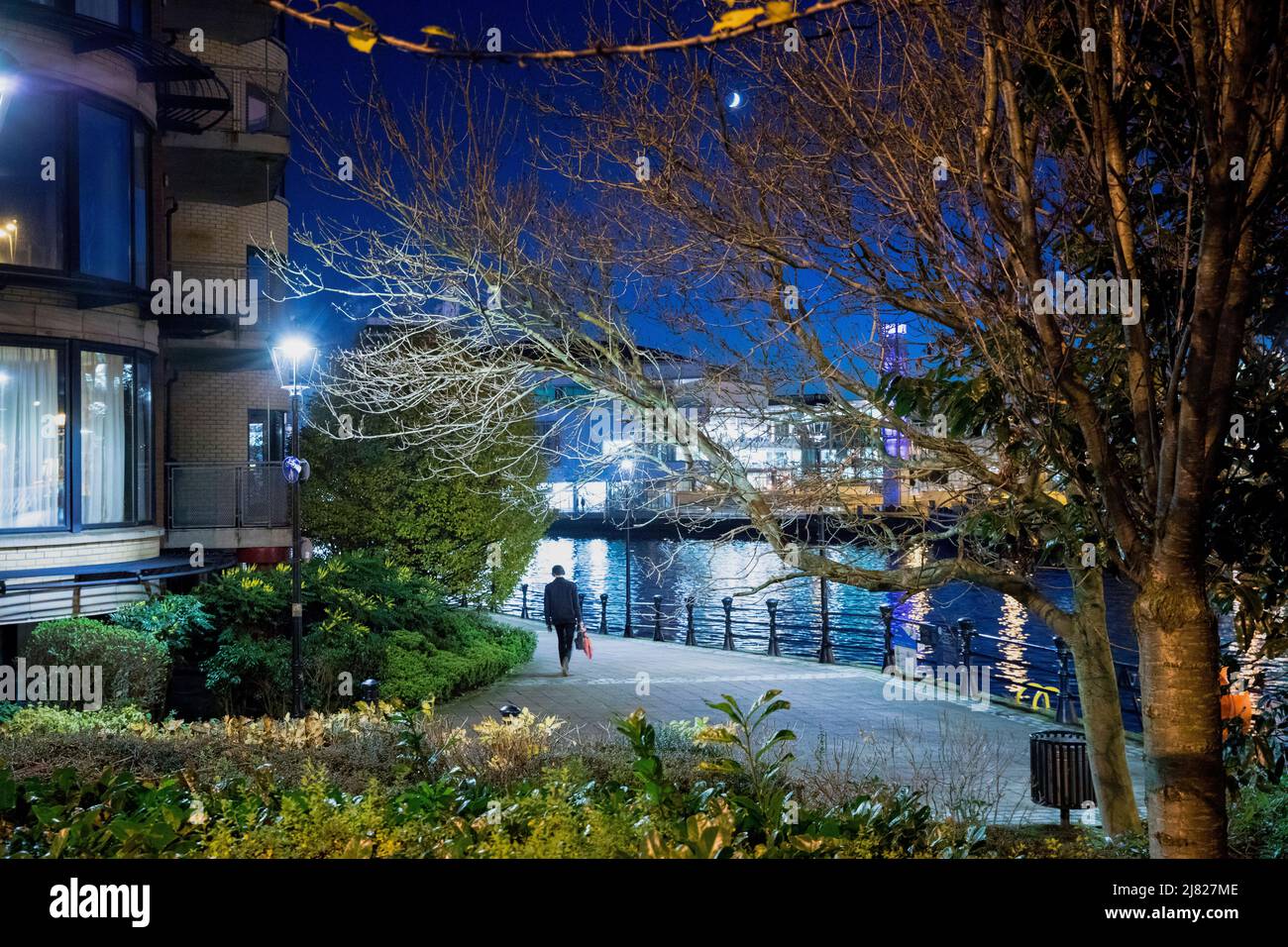 Lone commuter on riverside quays with city lighths in background at dusk, Belfast, Northern Ireland Stock Photo