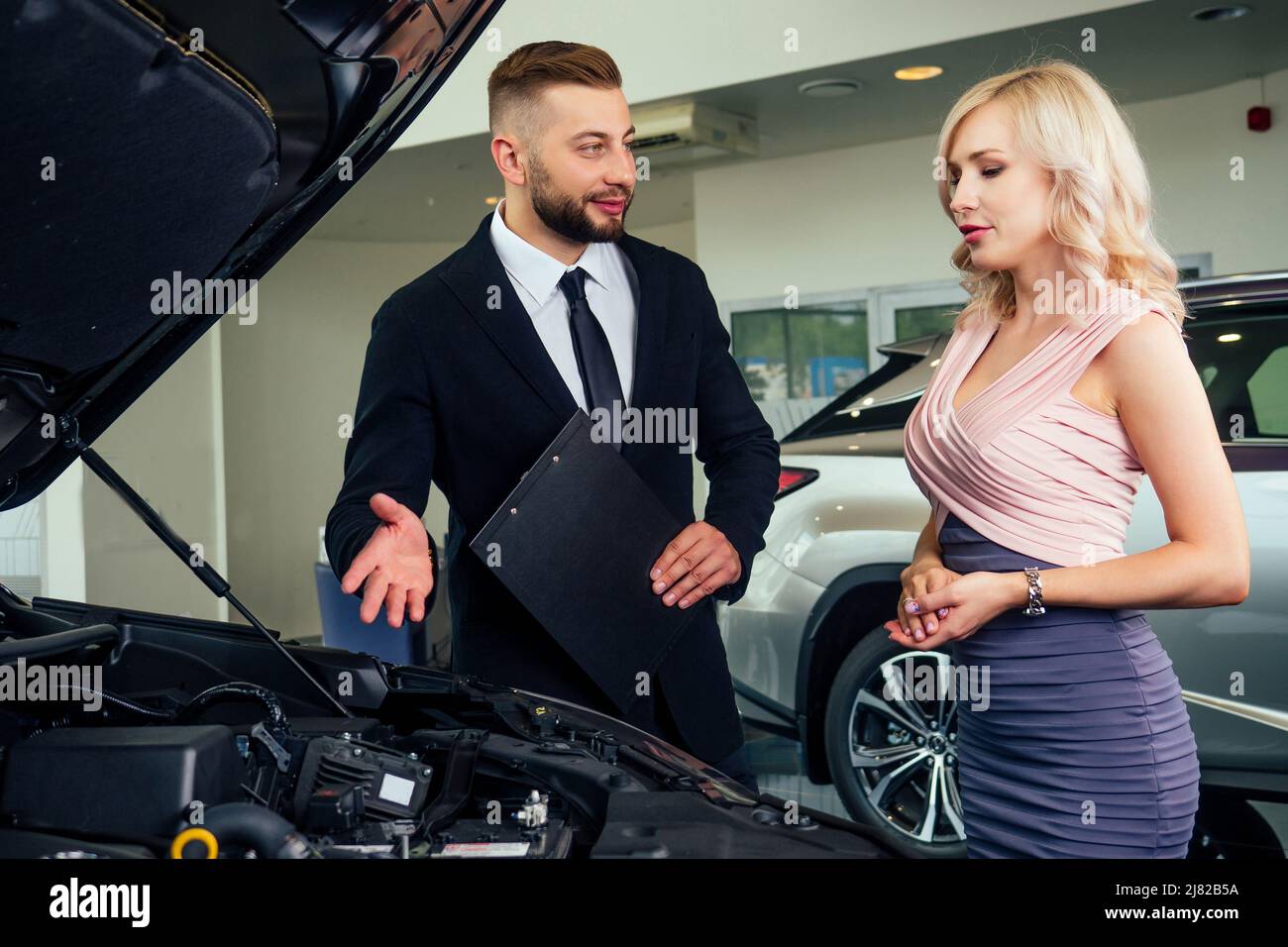 caucasian salesman in suit showing catalog to beautiful female blonde well-dressed customer in dealership salon Stock Photo