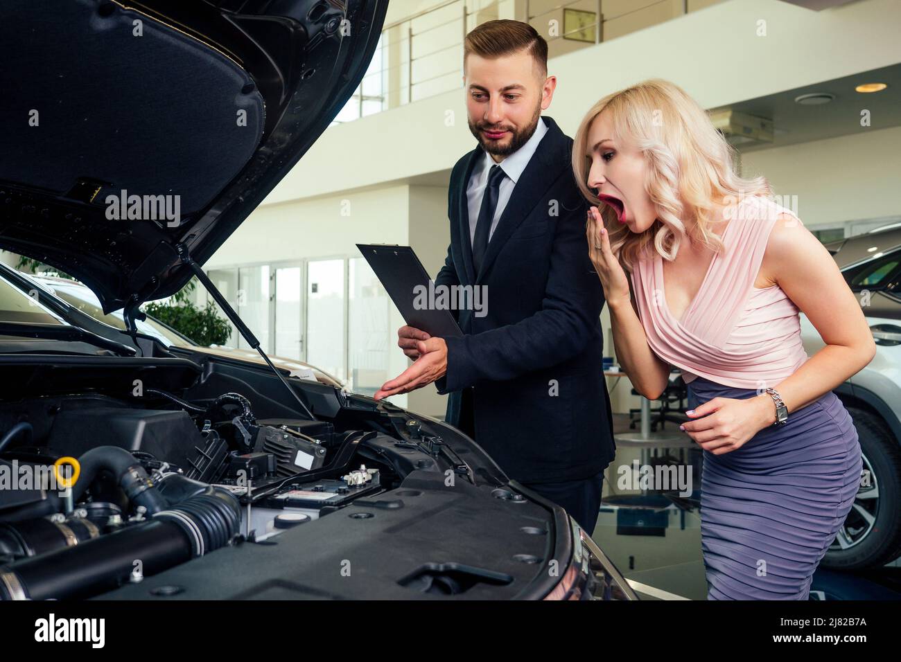 caucasian salesman in suit showing catalog to beautiful female blonde well-dressed customer in dealership salon Stock Photo