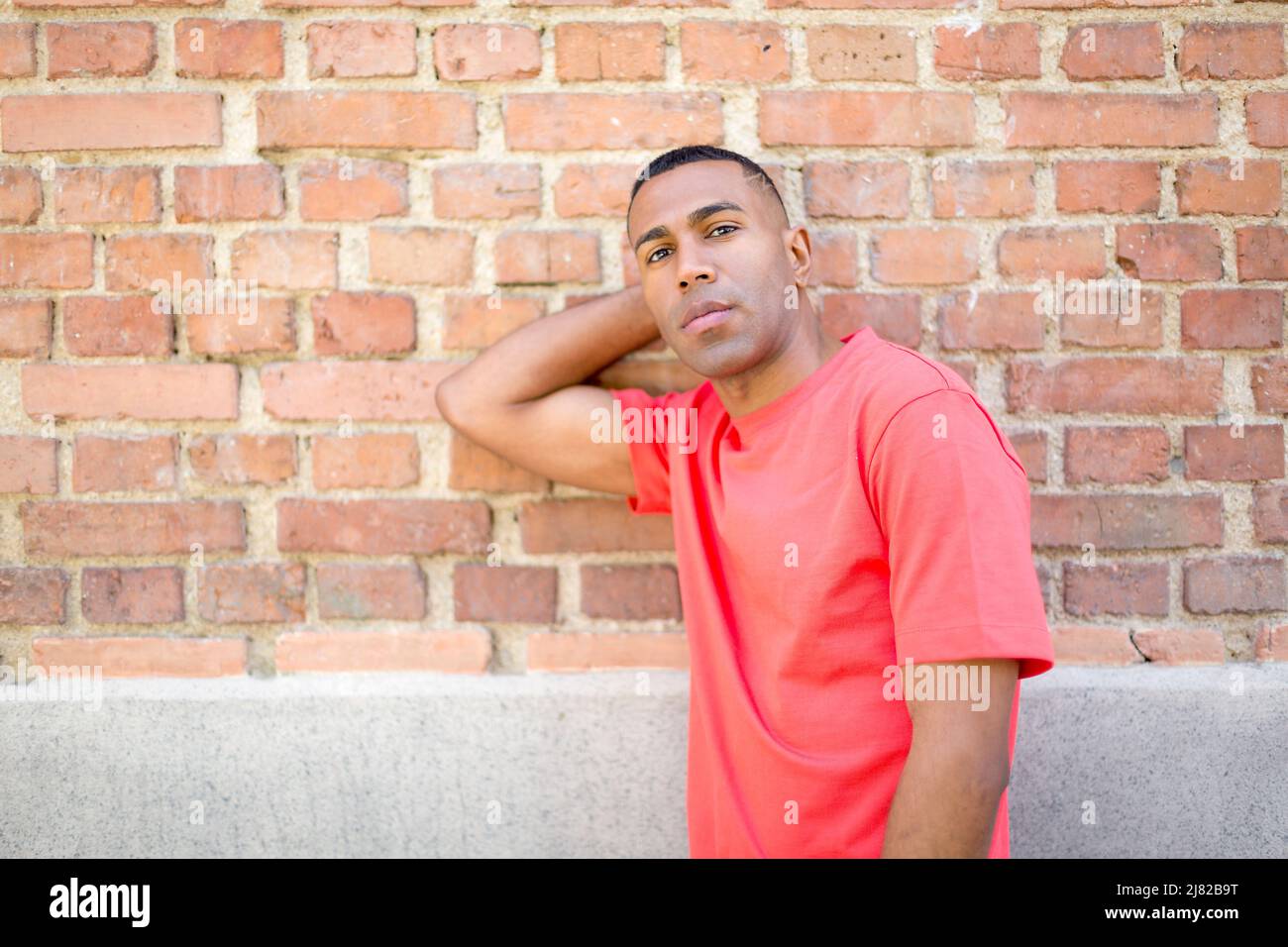 portrait young african american man looking at camera with hand on neck with wall in background vith copy space Stock Photo
