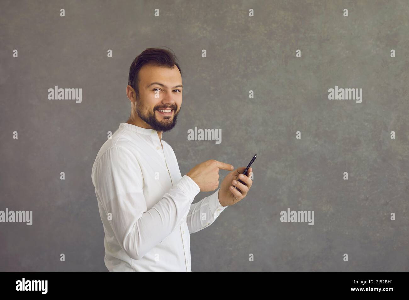 Happy young man using mobile phone standing isolated on grey copy space background Stock Photo