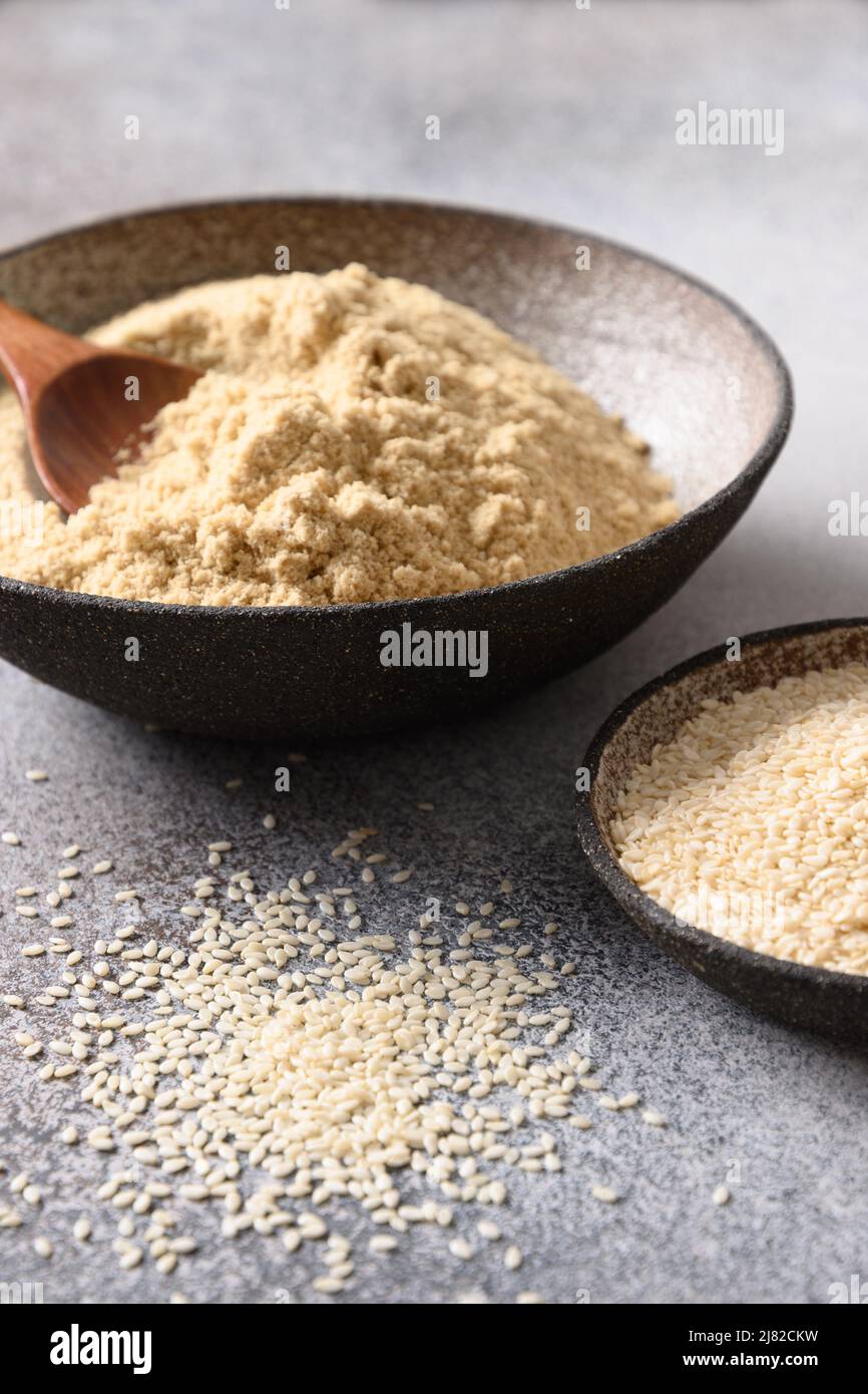 Sesame flour in bowl and seeds for clean eating gluten-free dessert and pastry on gray background. Vertical. Close up. Stock Photo