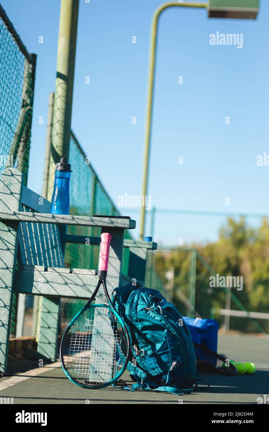 Tennis racket and backpack by empty wooden bench at court on sunny day Stock Photo