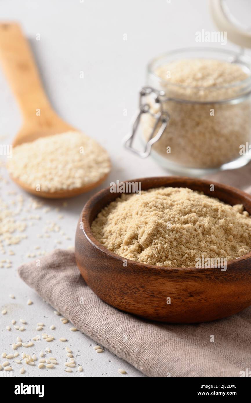 Sesame flour in wooden bowl and seeds in glass jar on white background. Vertical. Close up. Stock Photo