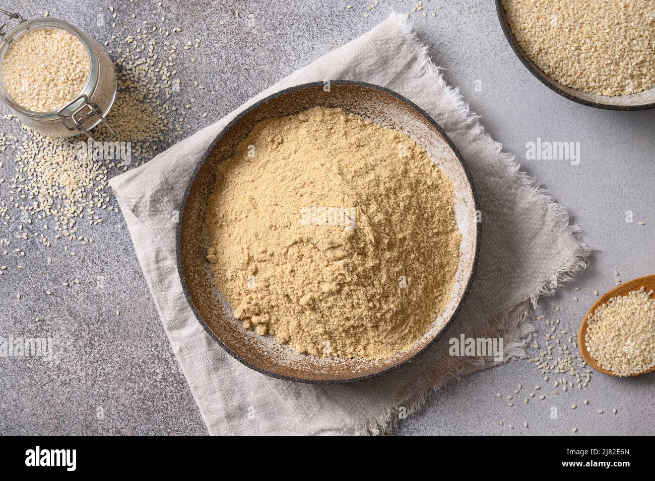 Sesame flour in bowl and white sesame seeds on gray background for cooking low carbohydrate dessert. Top view. Stock Photo