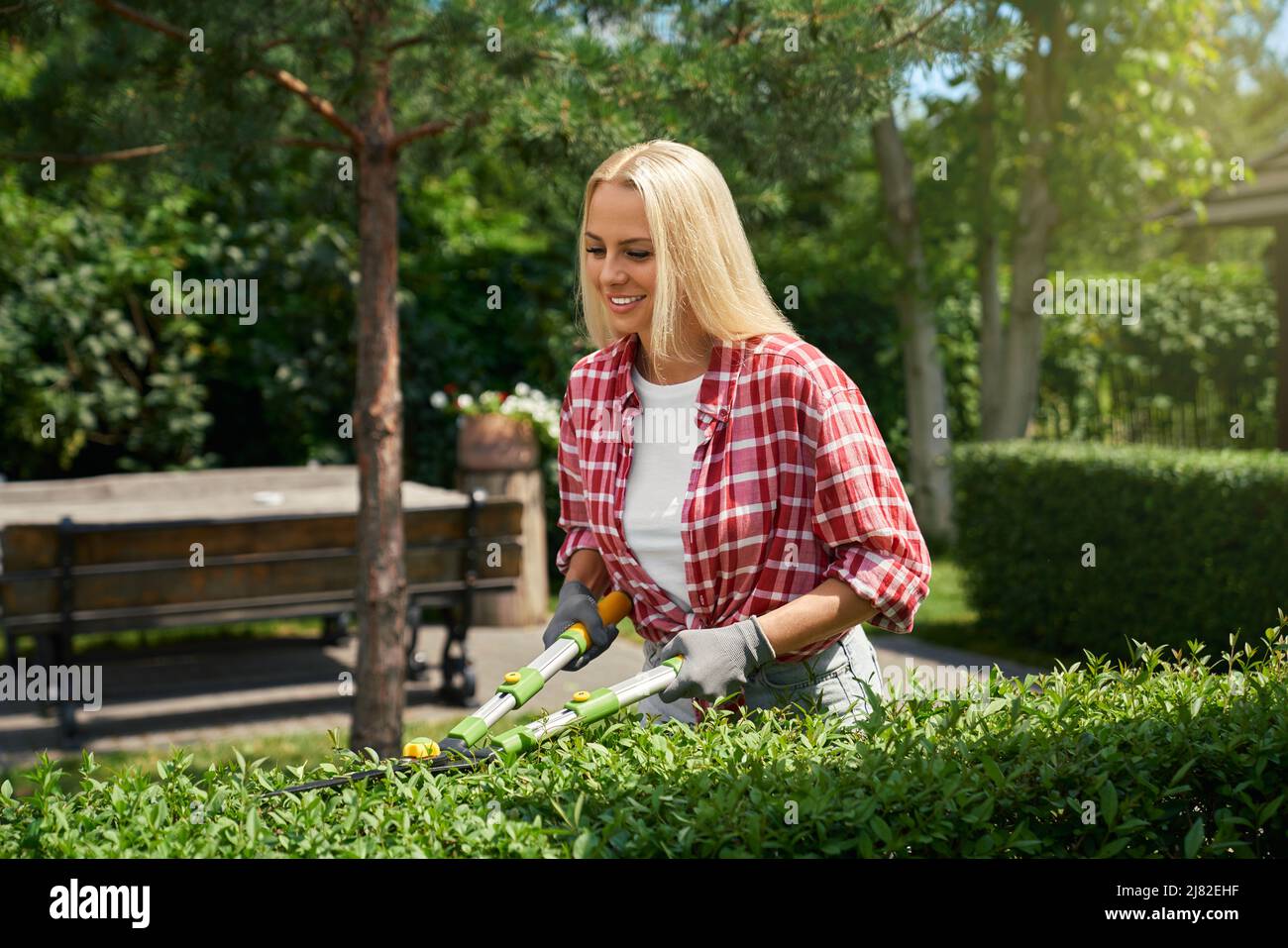 Smiling young woman with blond hair using branch scissors tool for