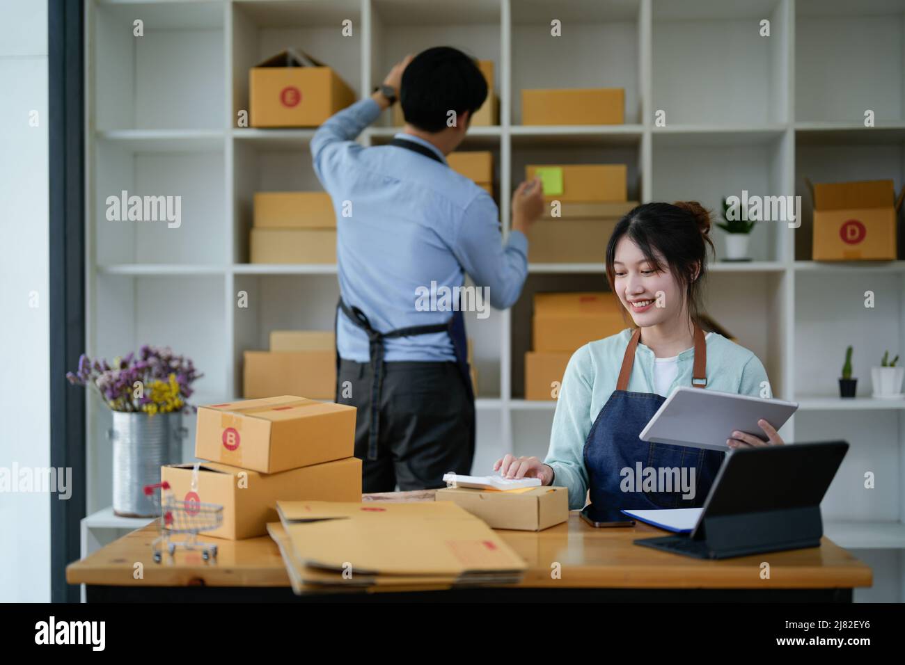 startup small business owner working with tablet at workplace. freelance man and woman seller check product order, packing goods for delivery to Stock Photo