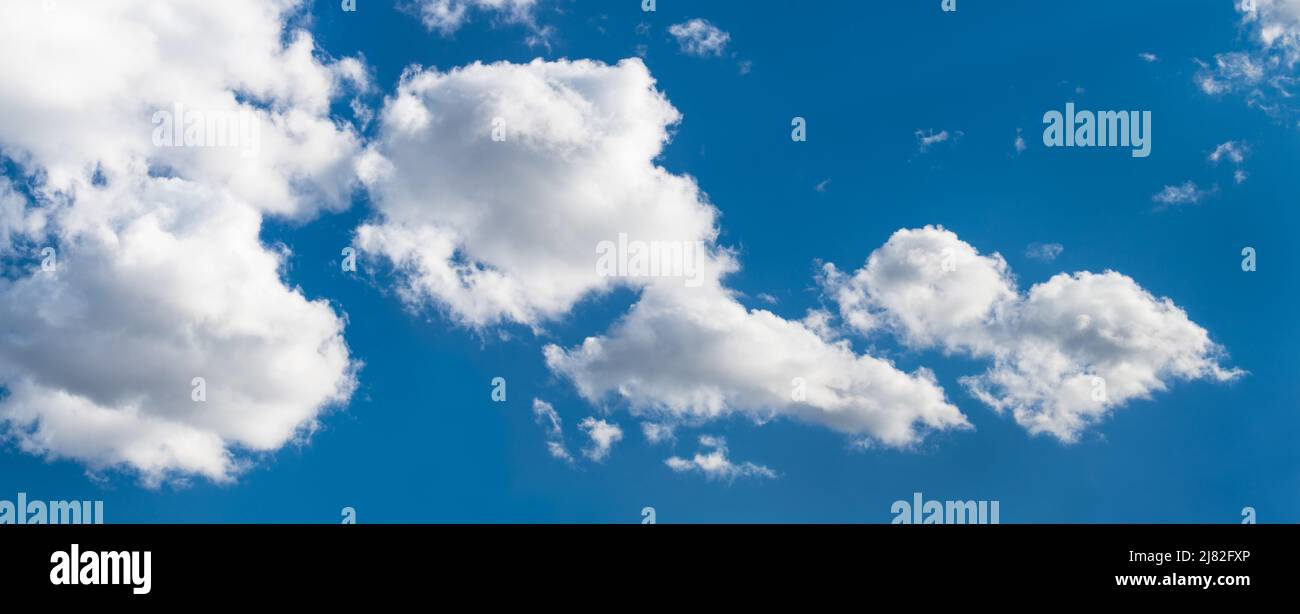 Sunlit white clouds on blue sky in abstract panoramic cloudscape background. Scenic panorama with beautiful group of fluffy cloud cumuli in hot summer. Stock Photo