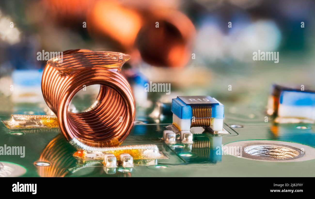 Orange wire winding of air-core coil and PCB electronic components in blurry background. Closeup of radio frequency inductor. Surface mount technology. Stock Photo