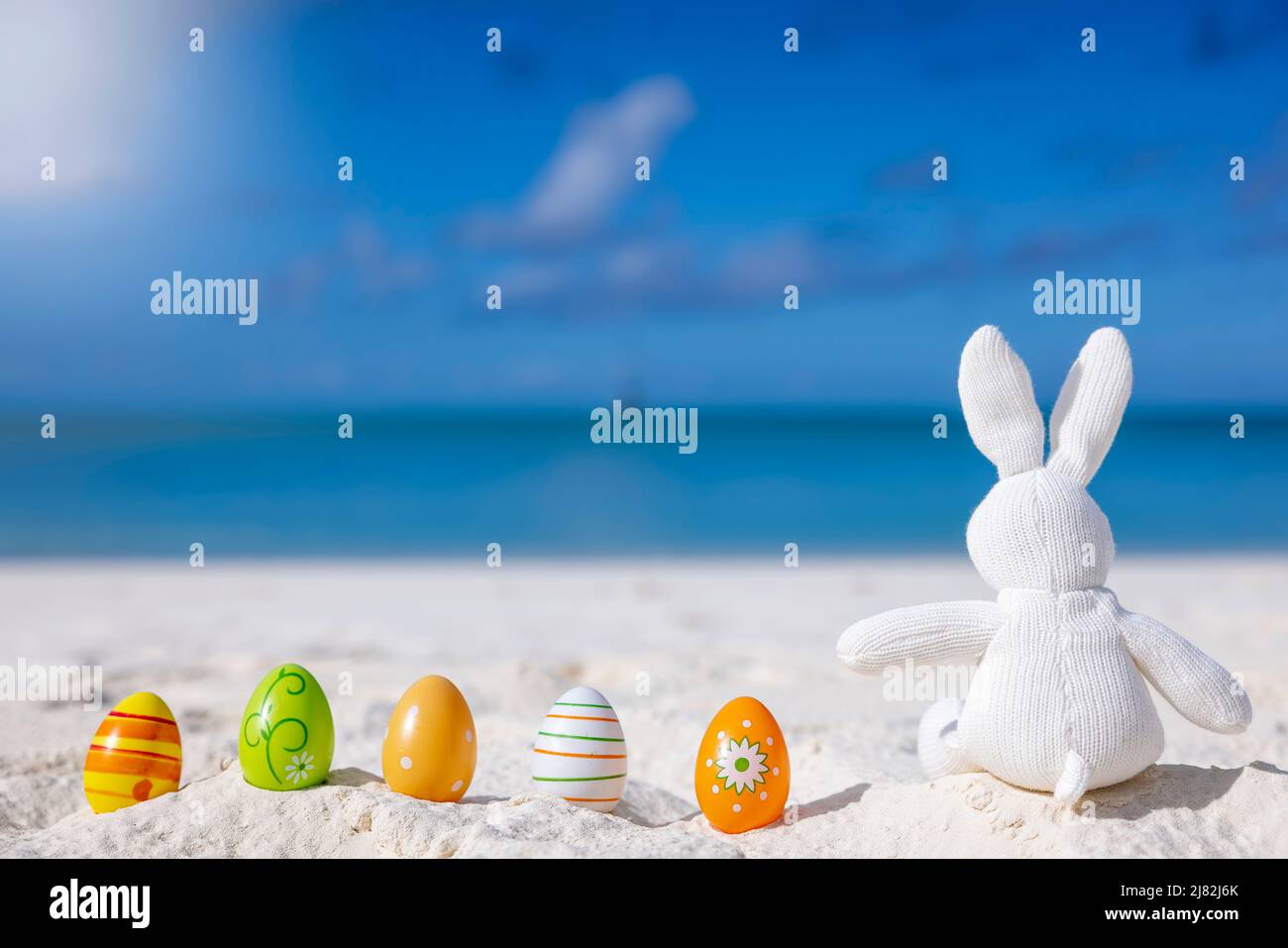 Easter travel concept with a bunny and colorful eggs sitting in the sand Stock Photo