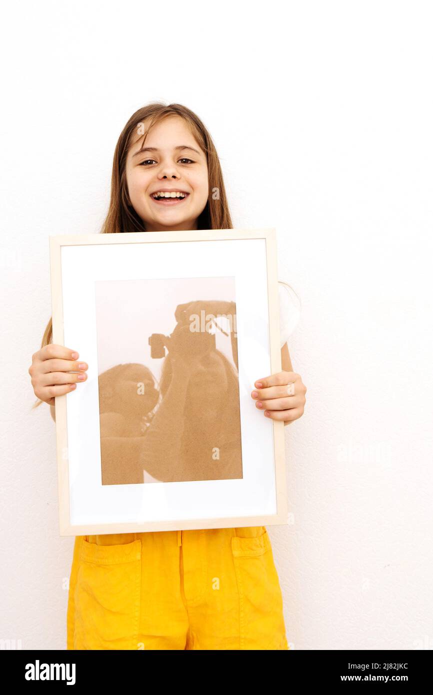 A young beautiful girl holds a frame with a picture in which the photographer's mother and the baby are reflected. The concept of family ,  Stock Photo