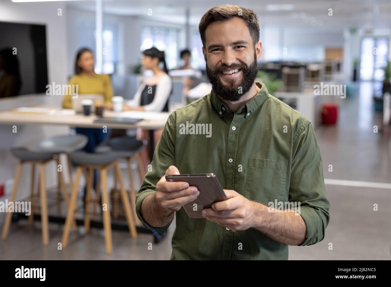 Portrait of smiling bearded businessman standing with digital tablet at ...