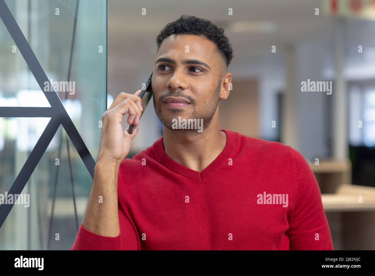 Thoughtful young hispanic businessman looking away while talking on smartphone Stock Photo