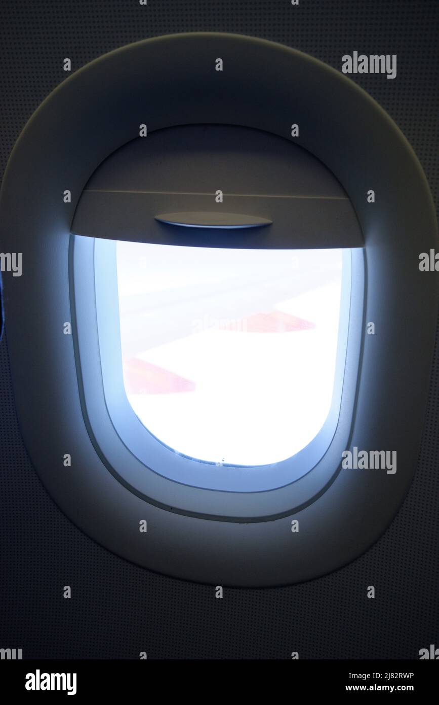 Aircraft cabin window porthole, with blind half drawn down. Stock Photo