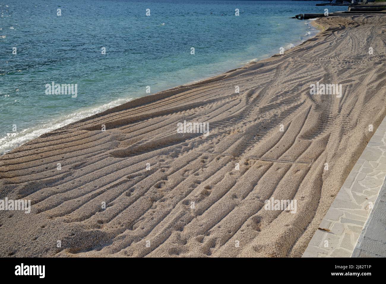 A new beach. Coarse sand/pebble/gravel product has just been delivered by lorry and pushed out by a wheel loader to form a beach by the sea. Stock Photo