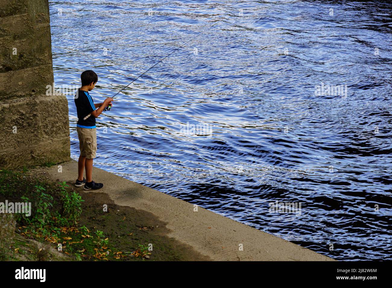 A casually dressed little boy is fishing in the summer in York, North Yorkshire, England, UK, while wearing shorts and a t-shirt. Stock Photo