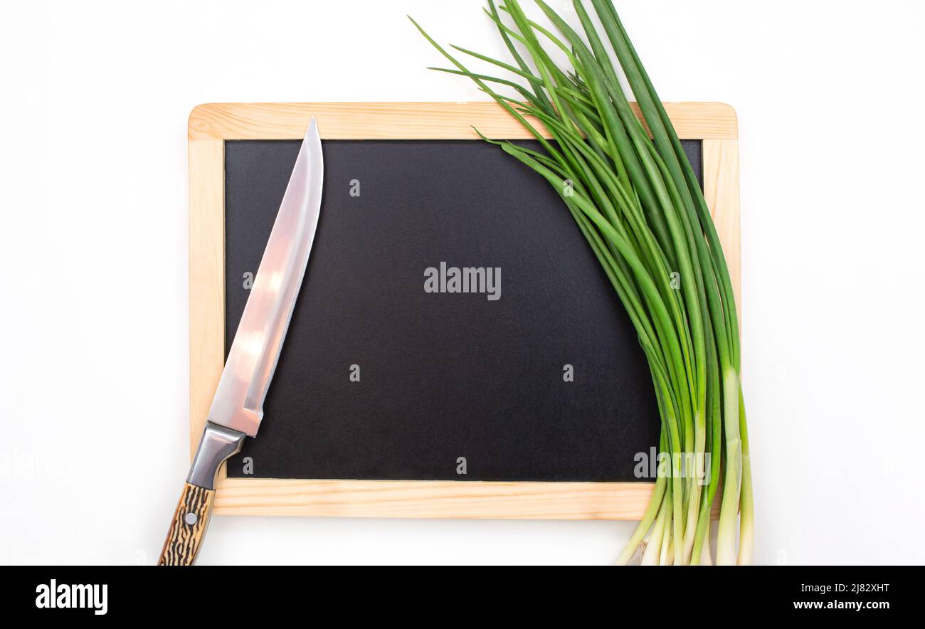 Green onion and knife on cutting black board on isolated background ...