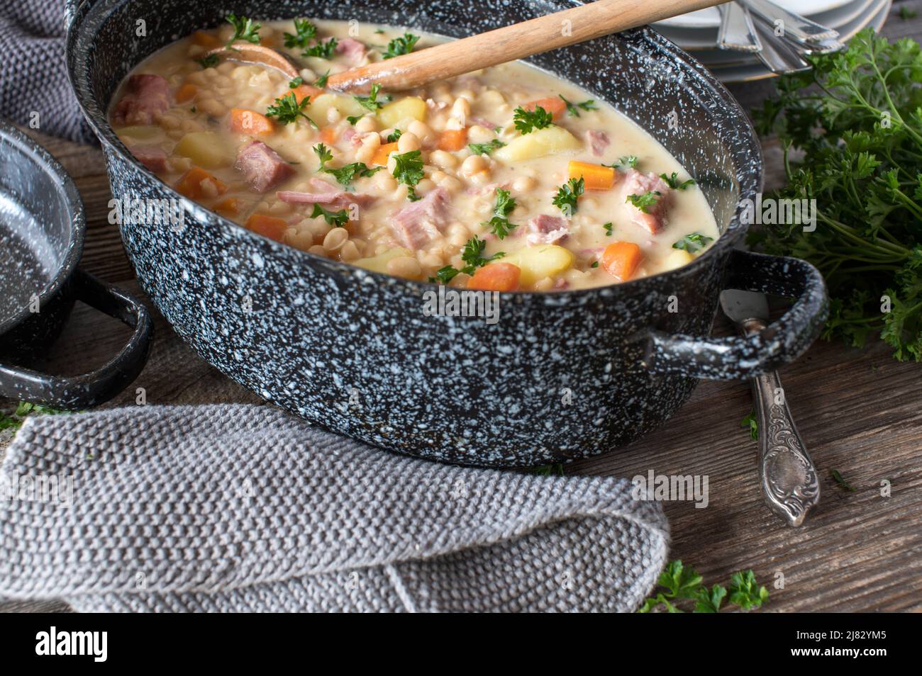 Rustic stew with white beans, vegetables, potatoes and pork meat in old-fashioned pot on wooden table Stock Photo