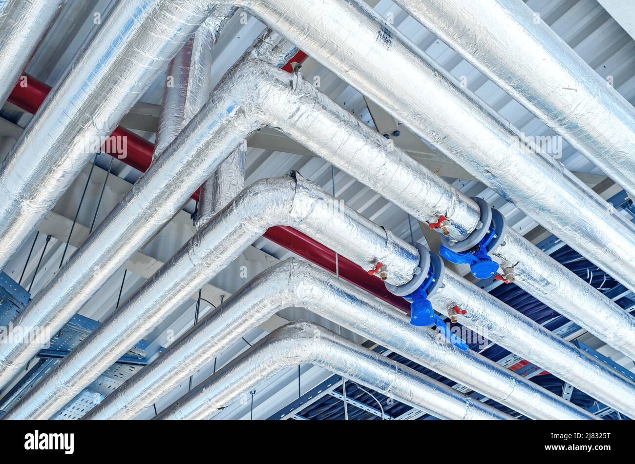 Metal pipes mounted under ceiling are covered with thermal insulation at modern production plant Stock Photo