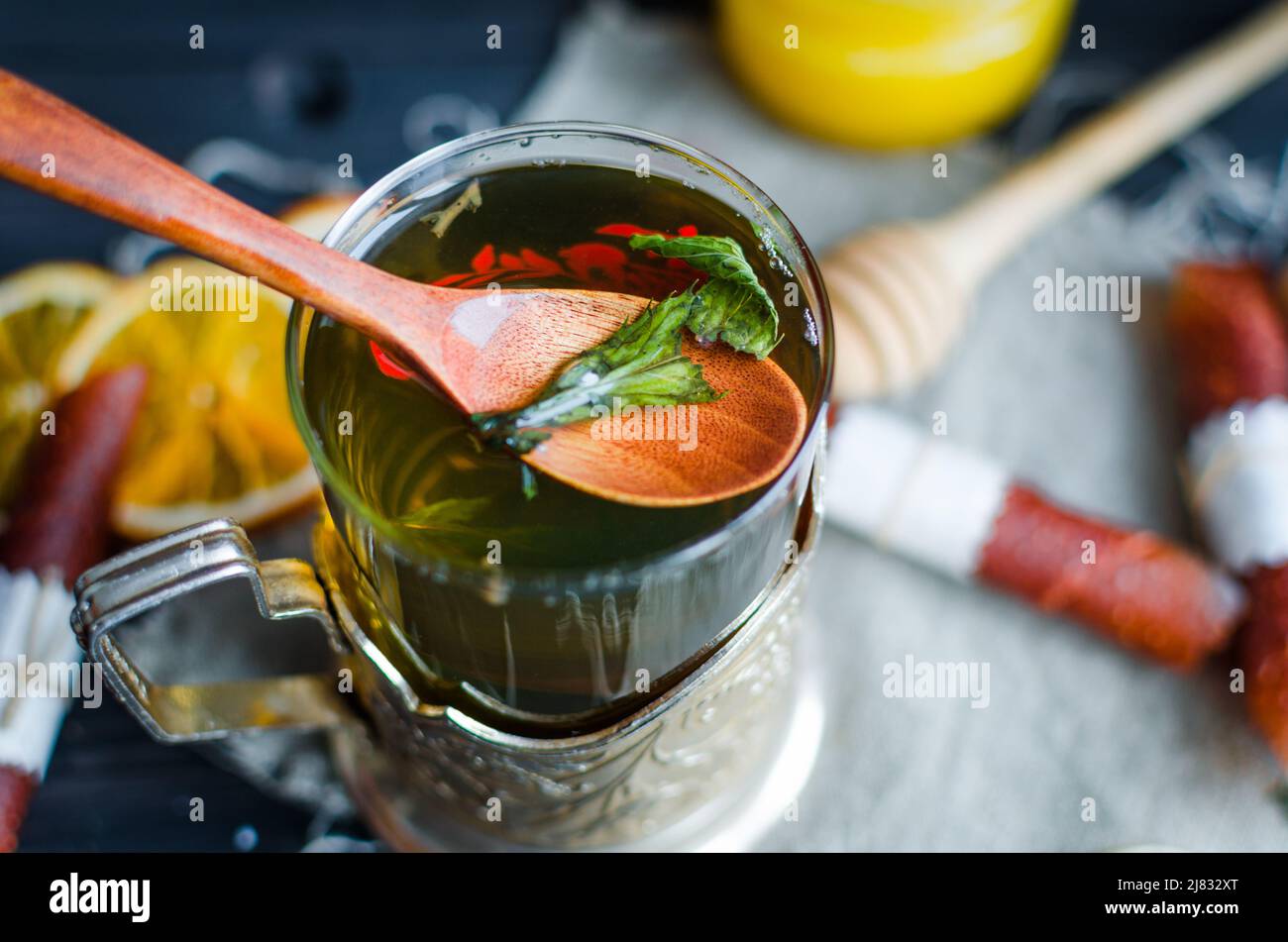 Cup of green tea  with mint,  lemon slice, dry fruits roll and tea mint leaves with strawberry in a wooden spoon on wooden background, copy space Stock Photo