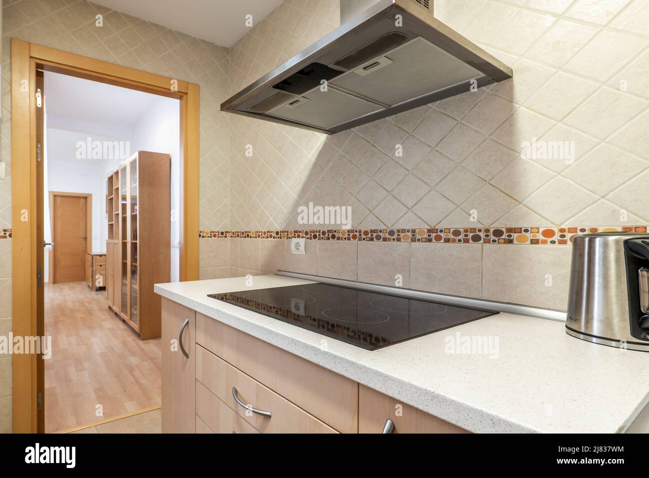 Kitchen with wood colored cabinets, rustic wall tiles and stainless steel range hood Stock Photo