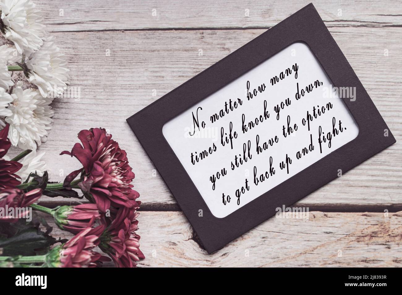 Motivational quote on chalkboard frame and white flowers on on wooden desk. Stock Photo