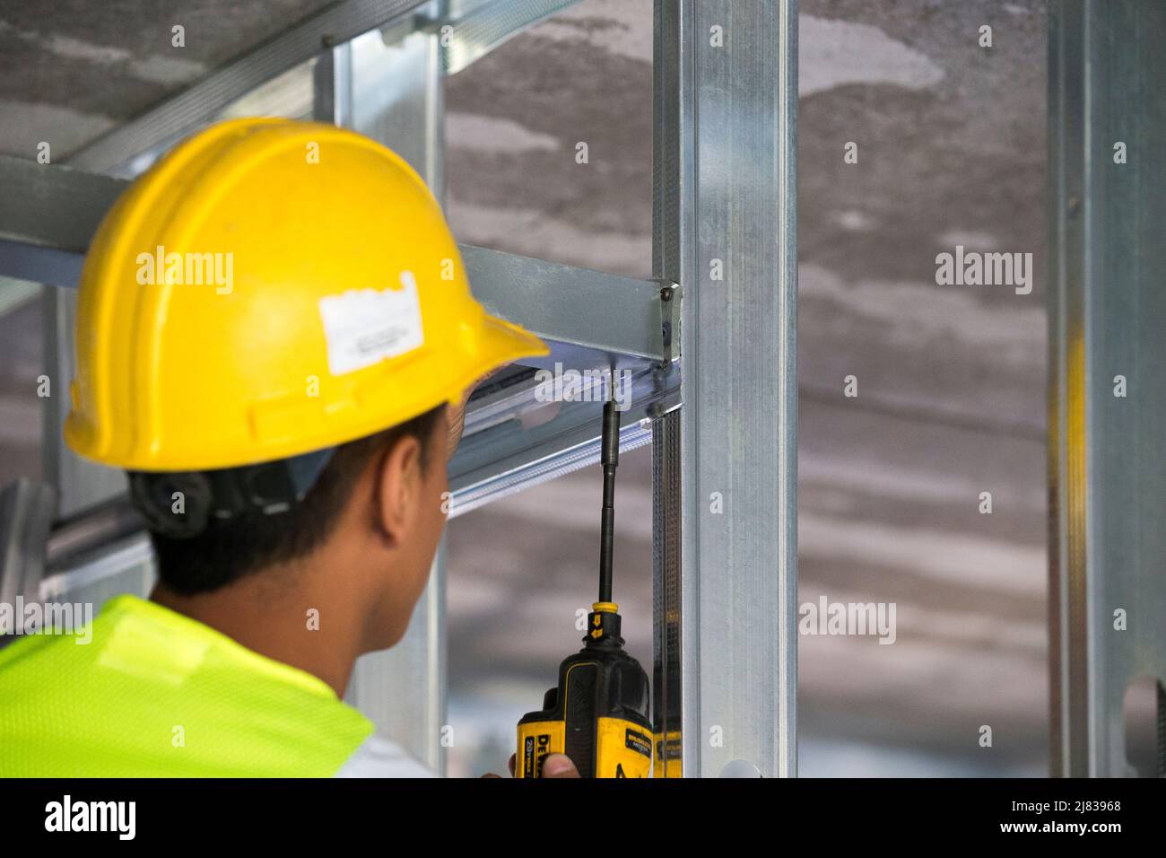 Skilled construction worker using an electric screwdriver to fasten a horizontal structural support beam to a vertical  steel supported  strut Stock Photo