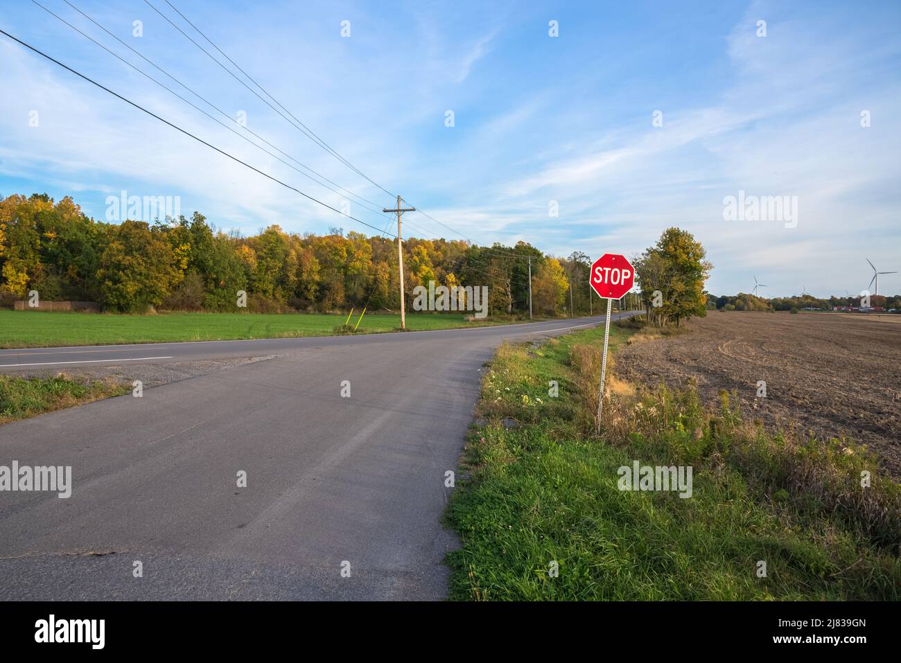 Stop sign at an intersection with a deserted country road at sunset. A wind farm is visible in background. Stock Photo