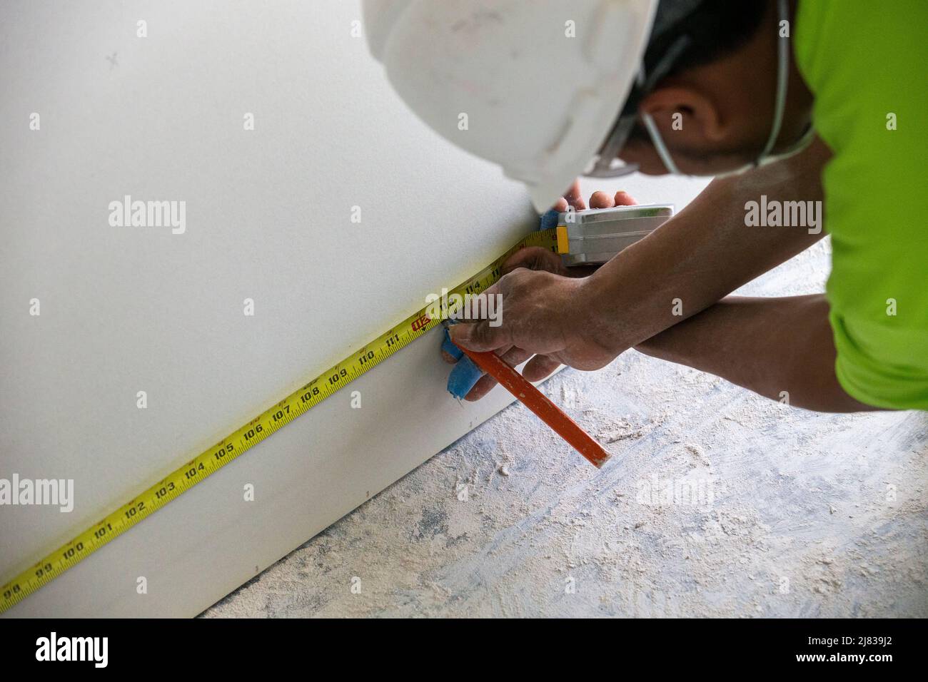 Drywall construction worker measuring and marking the drywall for
