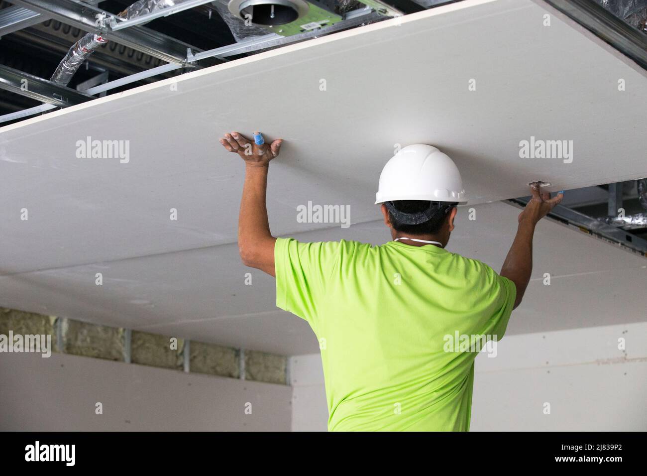 Drywall installer placing and fastening a large sheet of drywall on the