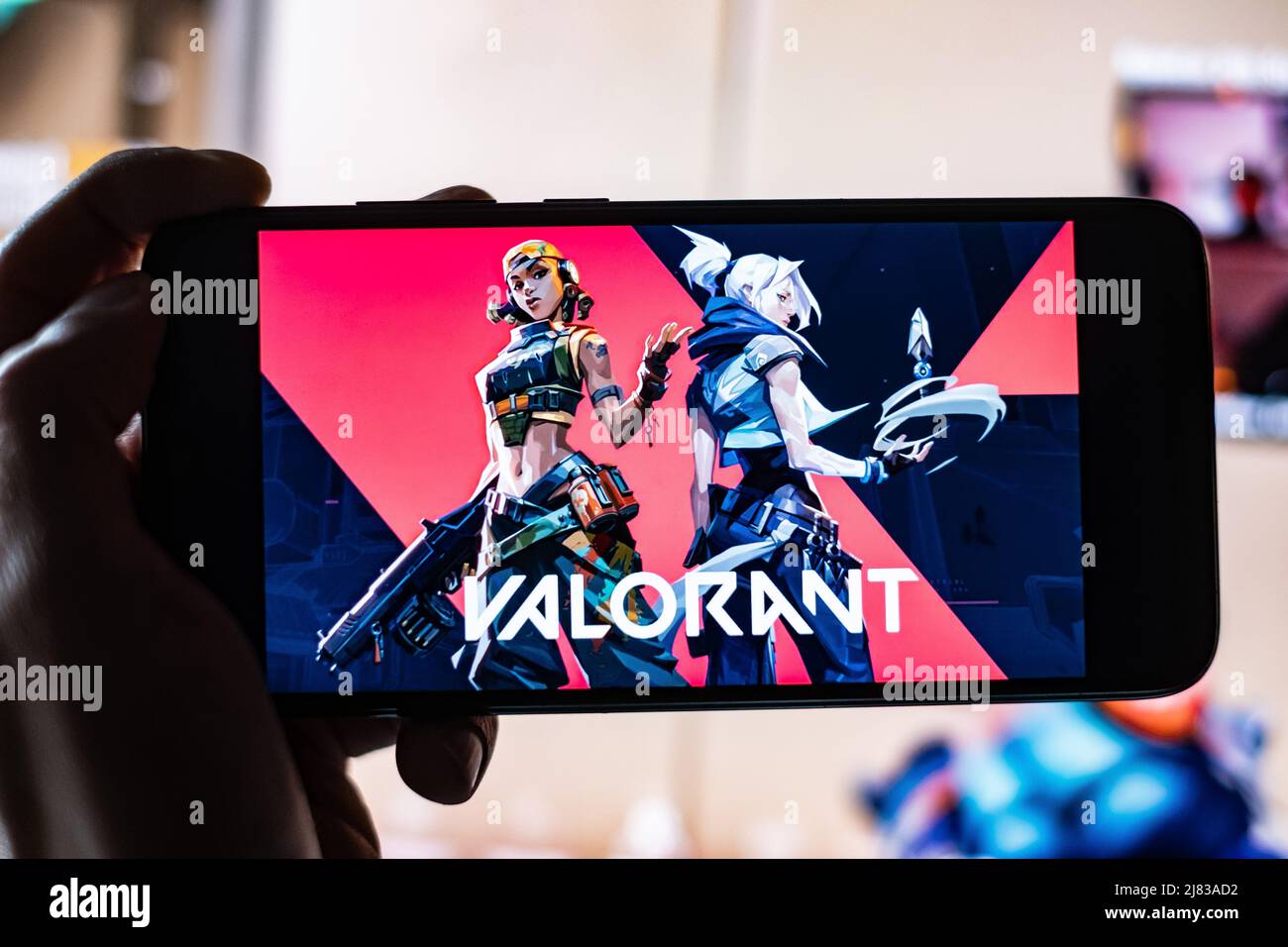 Valorant Game Title is shown on mobile phone Screen with twitch Streamer playing game in the background. A Game made by Riot Games in Los Angeles. Stock Photo