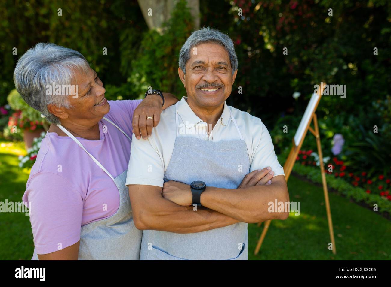 Smiling biracial senior woman with hand on husband's shoulder standing against plants in yard Stock Photo