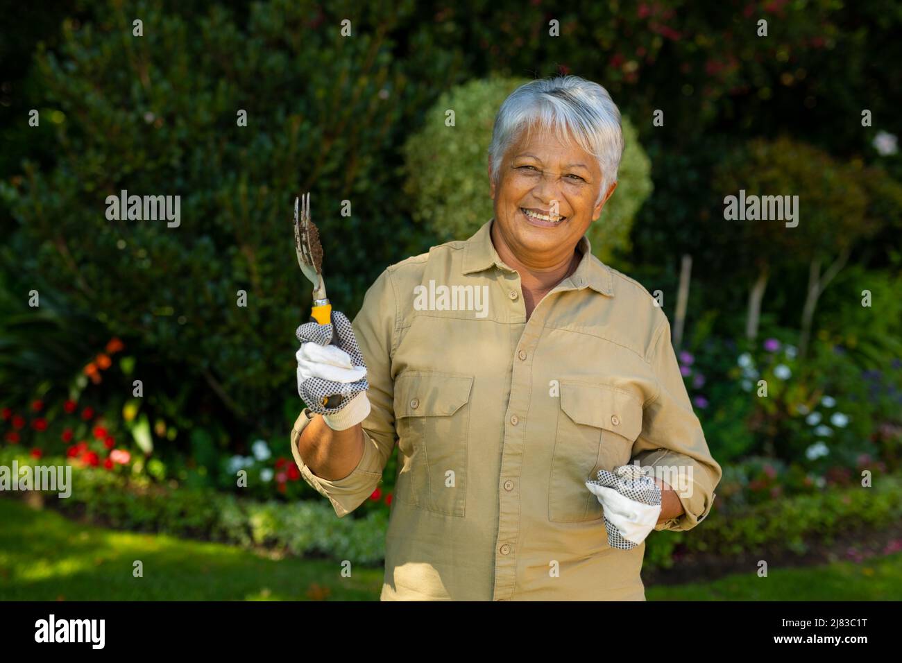 Portrait of smiling biracial senior woman with short hair wearing gloves and holding gardening fork Stock Photo