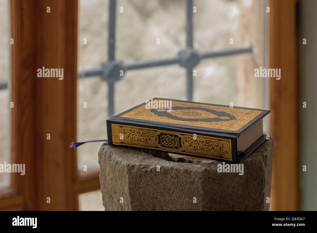 close up of the Quran book with black and gold binding on a stone plinth next to a bright window Stock Photo