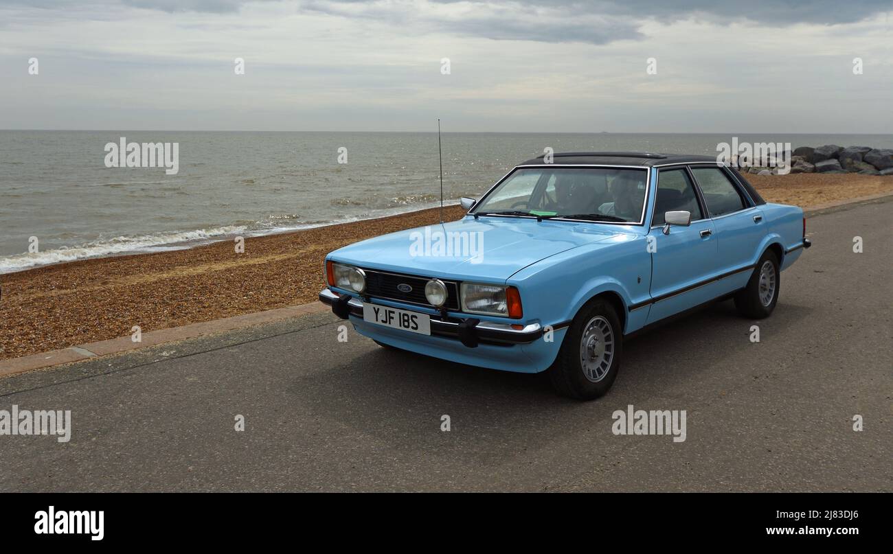 Classic Light Blue Ford Cortina Mk4 on seafront promenade beach and sea in background. Stock Photo