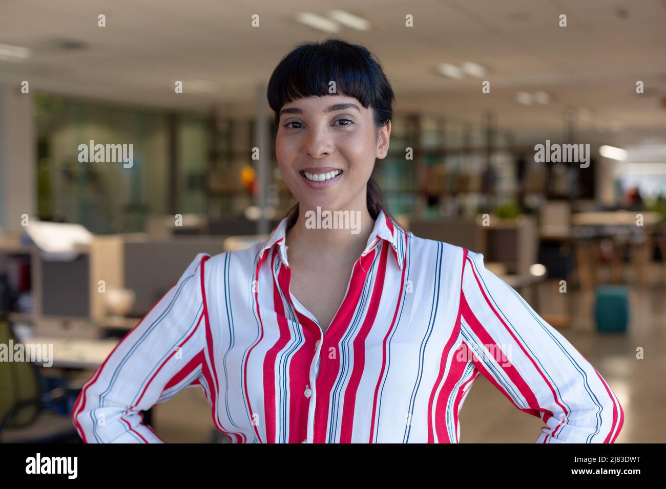 Portrait of happy young biracial female advisor with black bangs standing at modern workplace Stock Photo