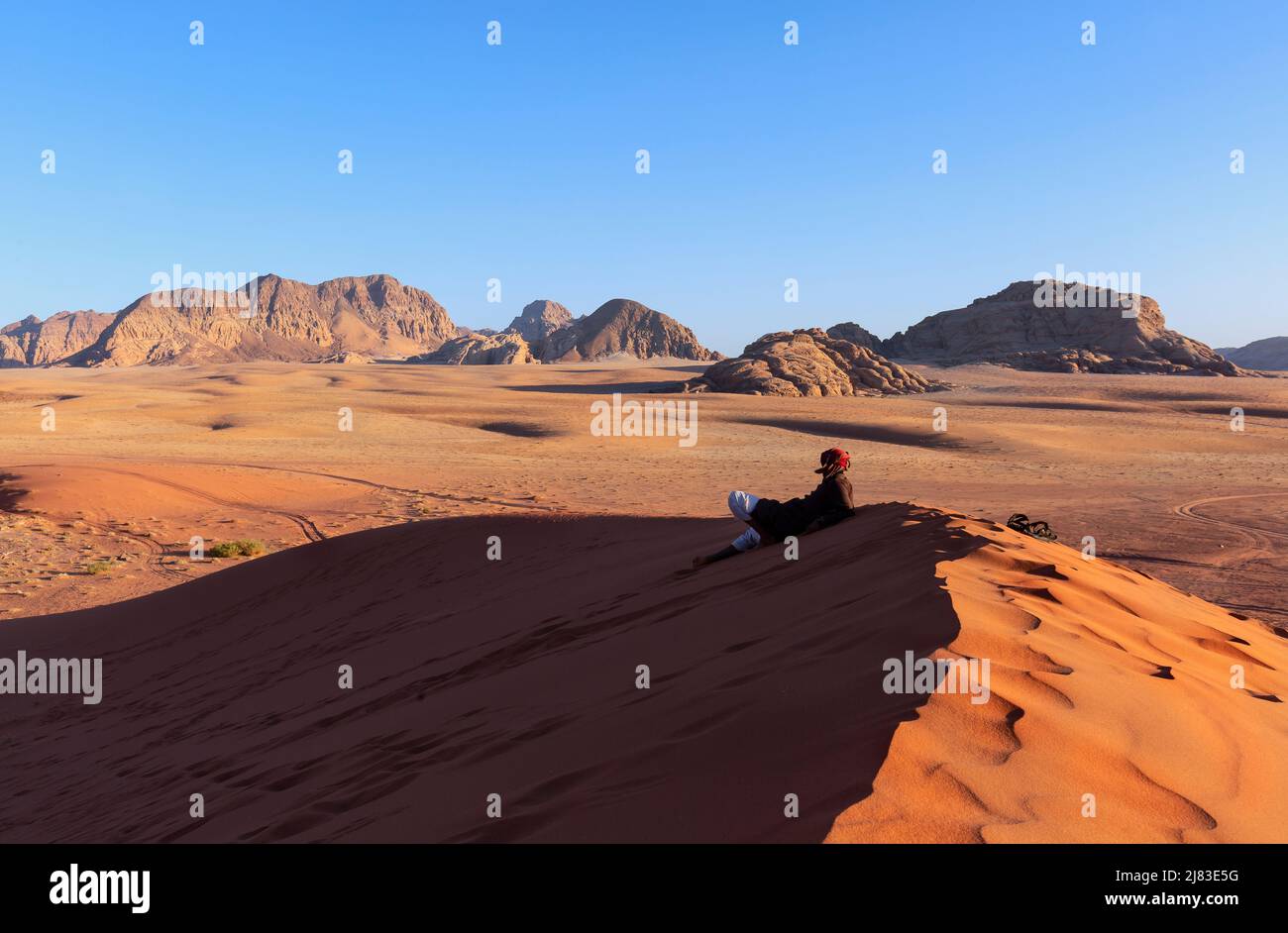 arab man in wadi rum desert sitting over a Dune in arabian Desert and admiring the landscape Stock Photo