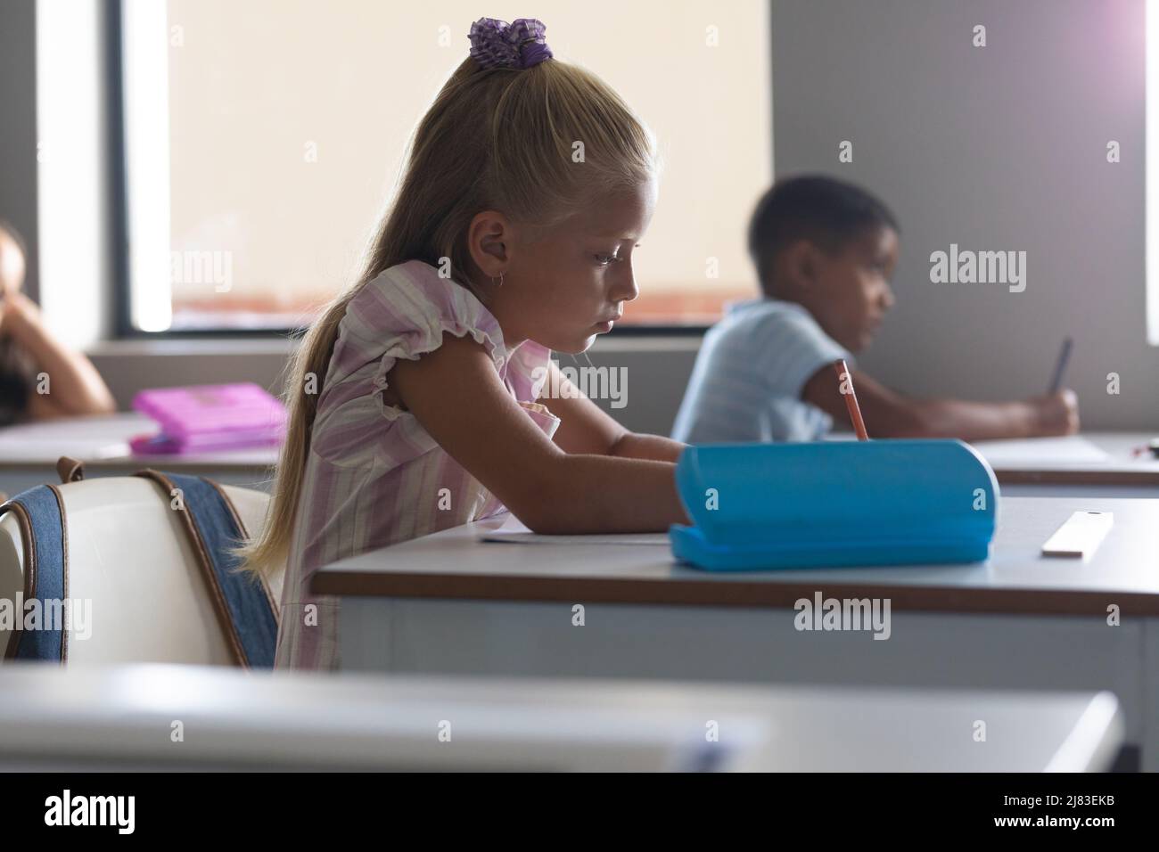 Multiracial elementary school students studying at desk in classroom Stock Photo