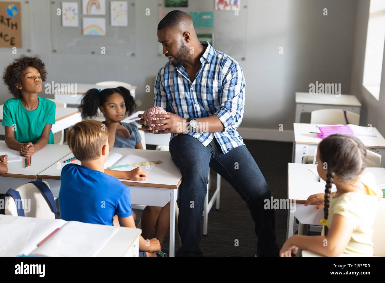 Multiracial elementary students looking at multiracial young male teacher explaining brain model Stock Photo