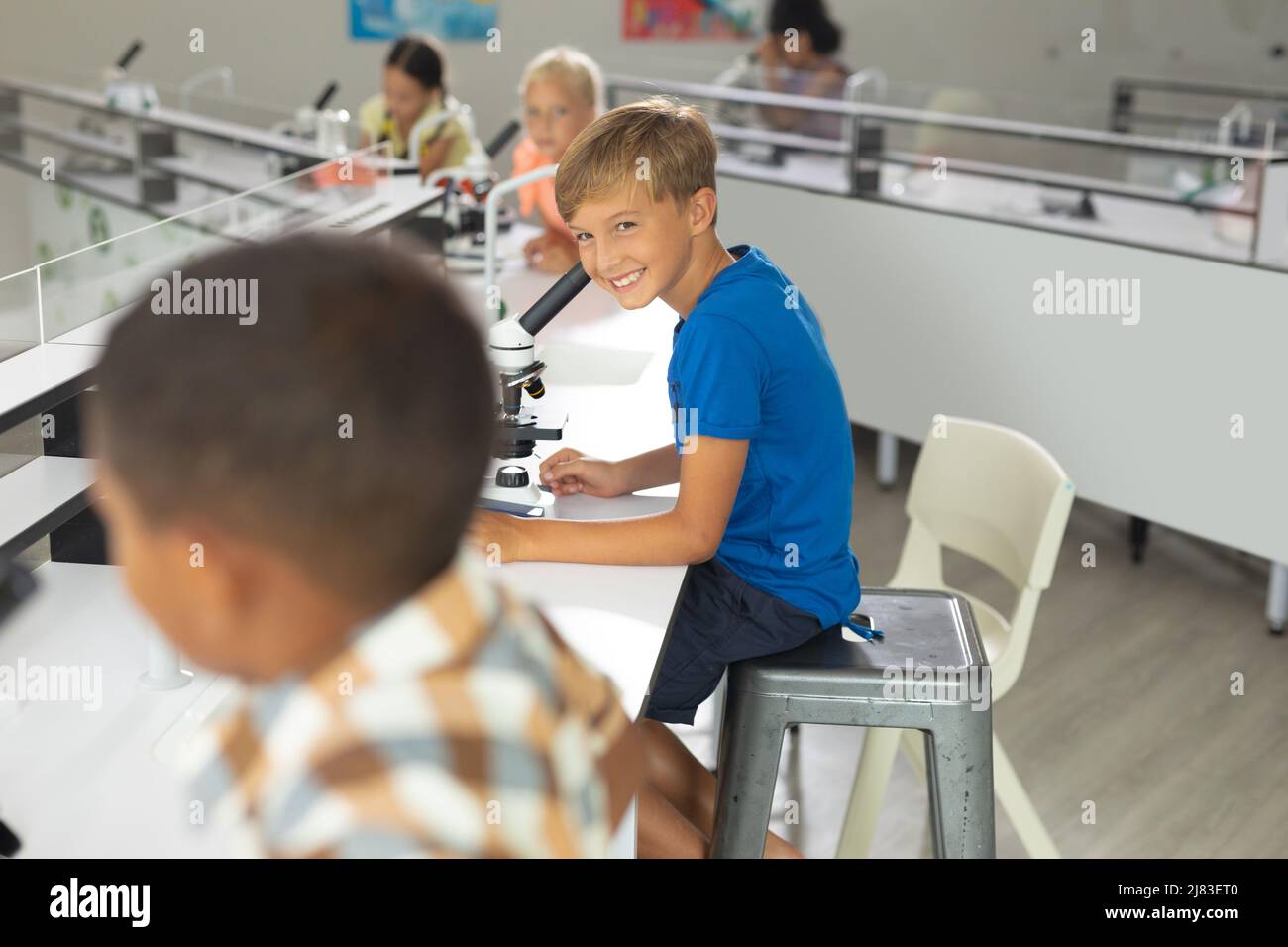 Smiling caucasian elementary boy looking at biracial male classmate in laboratory Stock Photo