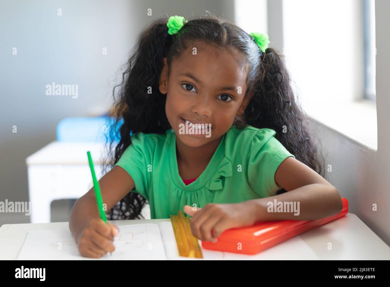 Portrait of smiling african american elementary schoolgirl with ponytails sitting at desk in class Stock Photo