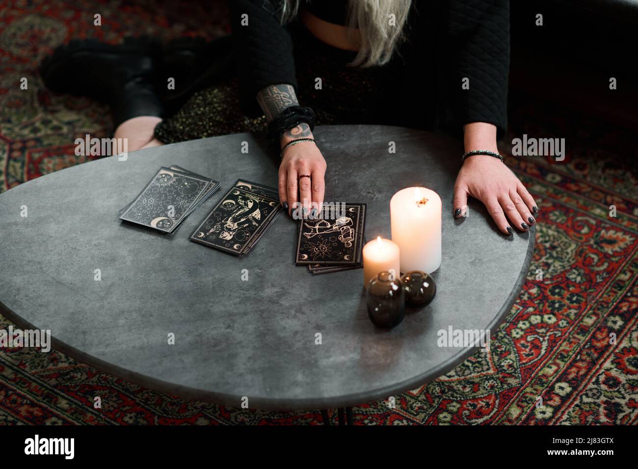 High angle of unrecognizable mature woman with long gray hair sitting on floor in living room reading tarot cards Stock Photo