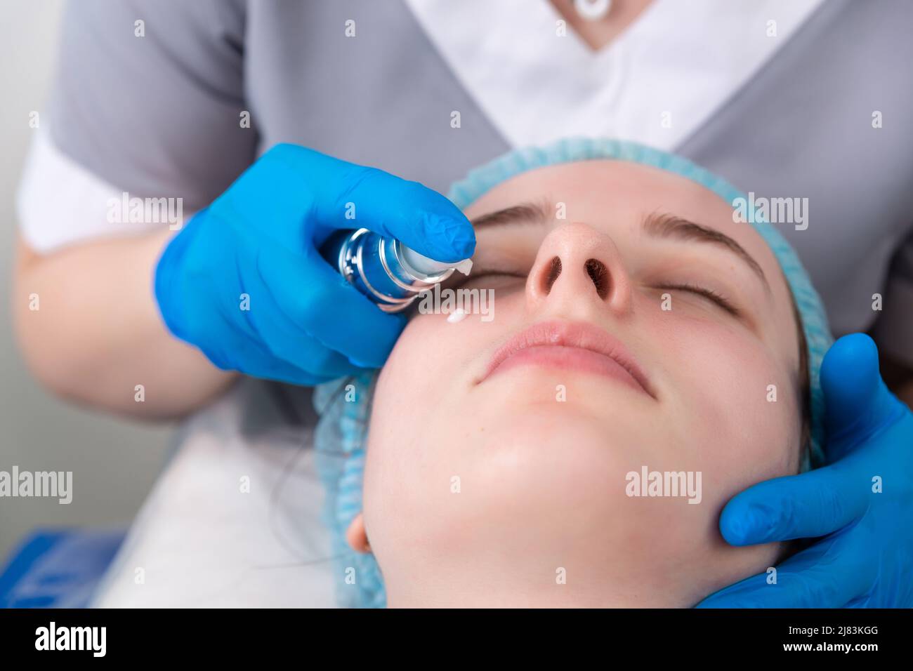 Face skin cream treatment or therapy for tired face skin. Dermatologist applying cream on female face skin. Stock Photo