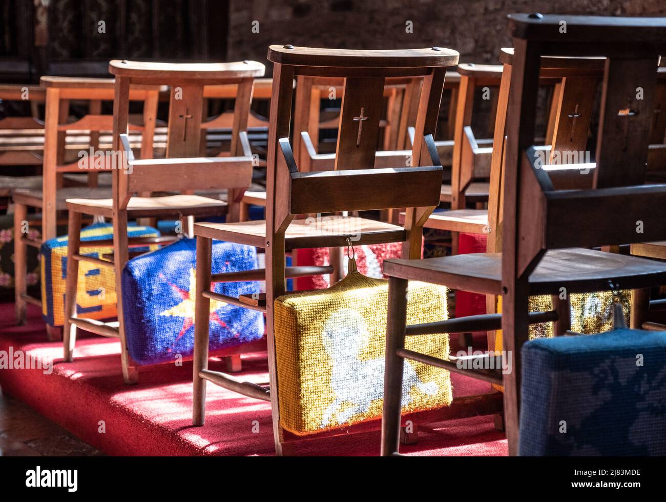 Embroided prayer cushions on the back of wooden chairs in Cockington Court Church, Devon Stock