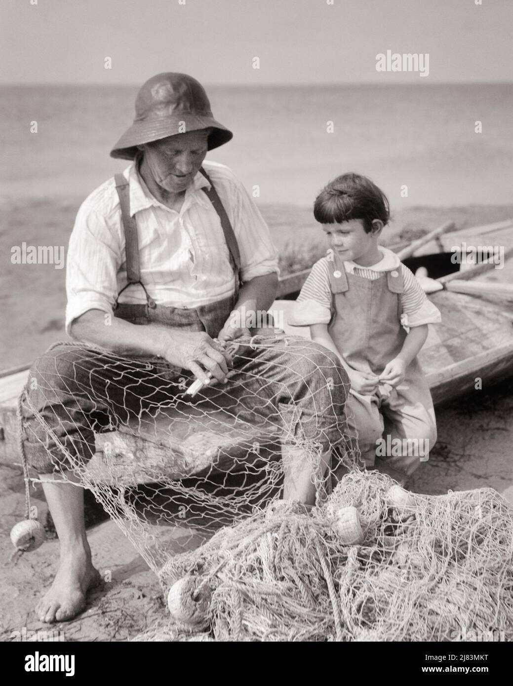 1920s YOUNG BOY SITTING ON BOAT BESIDE SENIOR MAN FISHERMAN WEARIING A SOU’WESTER HAT REPAIRING HIS FISHING NETS - j279 HAR001 HARS ELDER FISHERMAN RURAL COPY SPACE YOU FRIENDSHIP HALF-LENGTH PERSONS INSPIRATION MALES B&W HAPPINESS OLD AGE OLDSTERS HIGH ANGLE OLDSTER HIS KNOWLEDGE NETS YOUNG AND OLD ELDERS REPAIRING CONNECTION CONCEPTUAL BESIDE ELDERLY MAN GROWTH JUVENILES TOGETHERNESS YOUNGSTER BLACK AND WHITE CAUCASIAN ETHNICITY HAR001 OLD FASHIONED Stock Photo